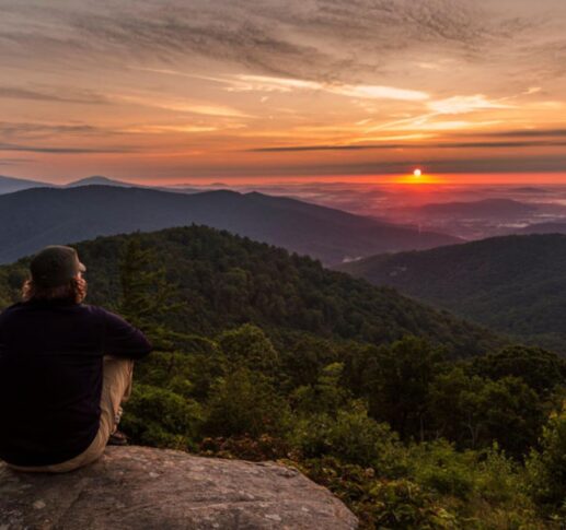 Hiker sitting on a rock looking over mountains at sunset.