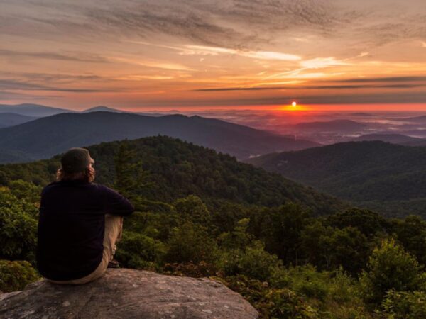 Hiker sitting on a rock looking over mountains at sunset.